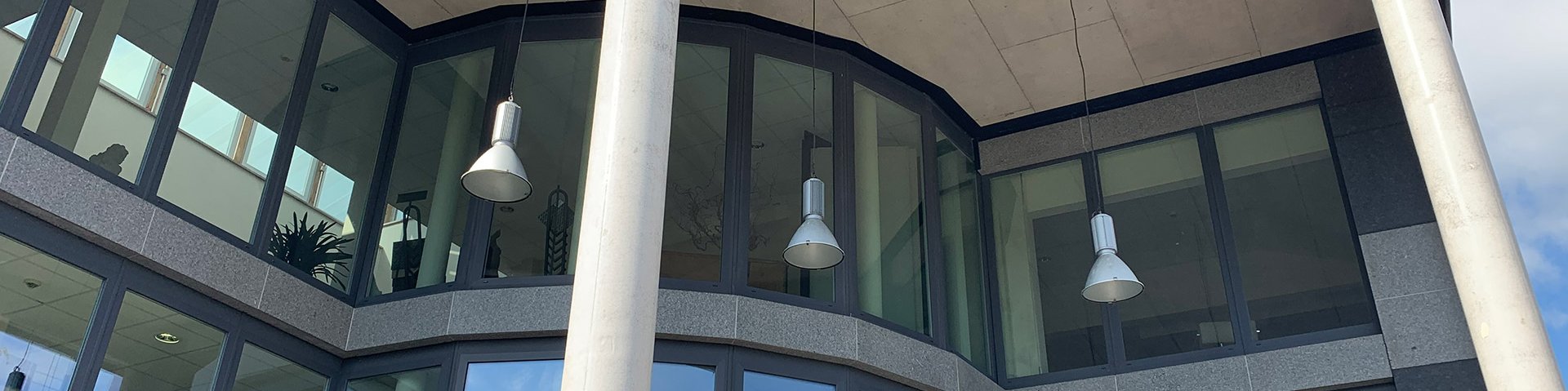 Vorderansicht eines Gebäudes mit einer Glasfront. Von oben hängen Lampen runter