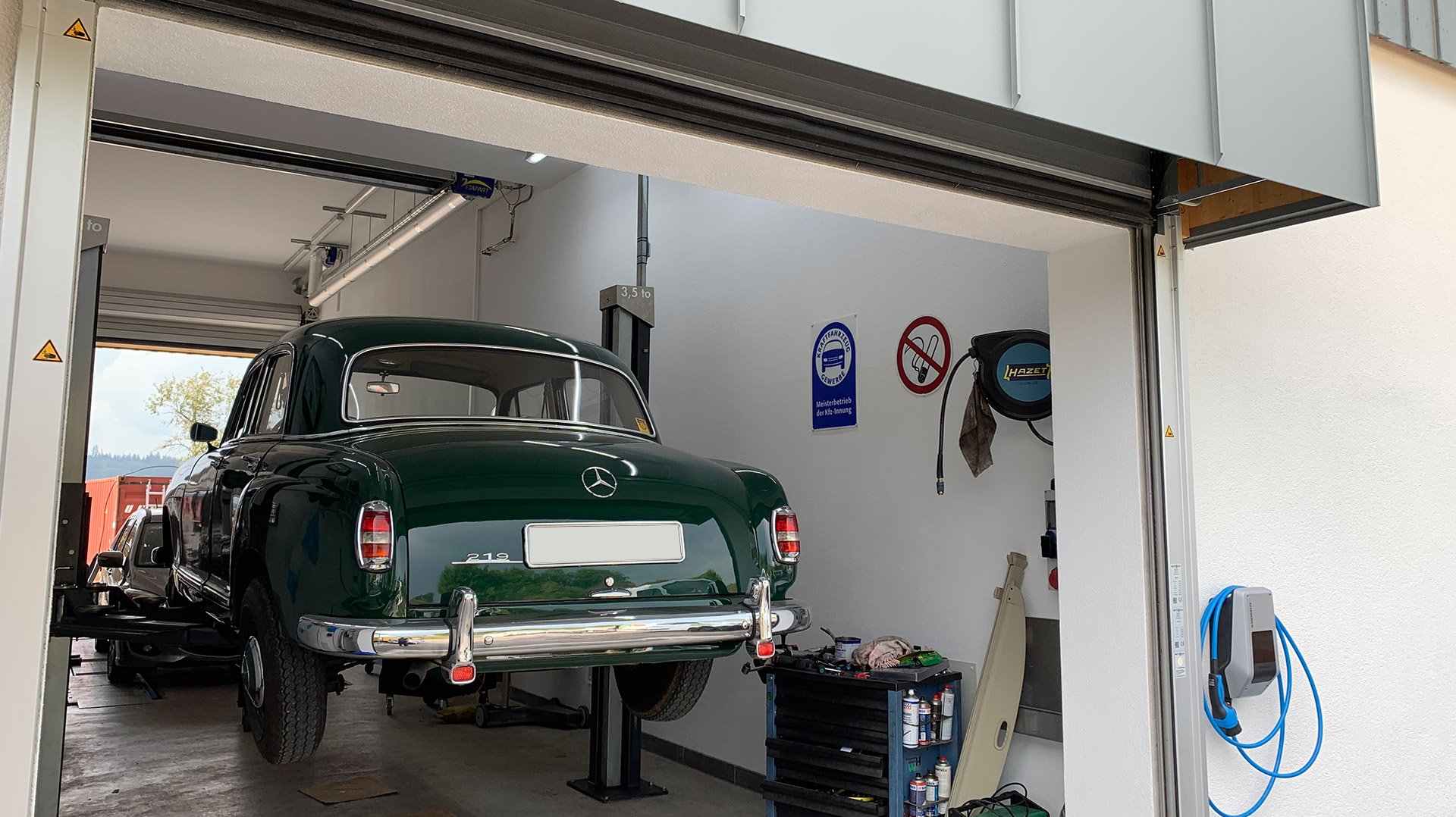 Ein grünes Auto befindet sich auf einer Hebebühne in einer KFZ Werkstatt