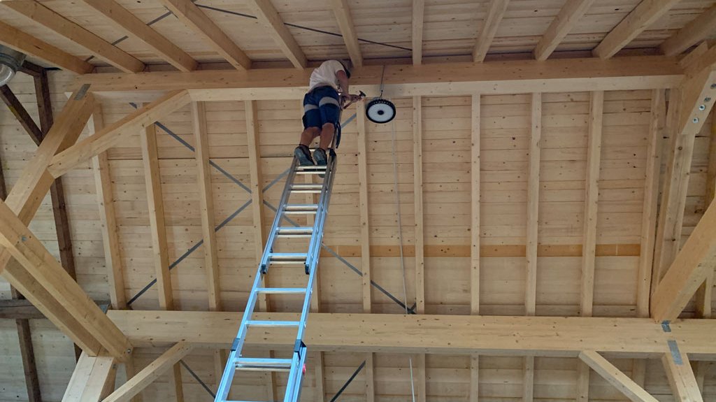 Beleuchtungstechnik: Techniker beim Anbringen eines Hallenstrahlers im Dachstuhl einer Halle